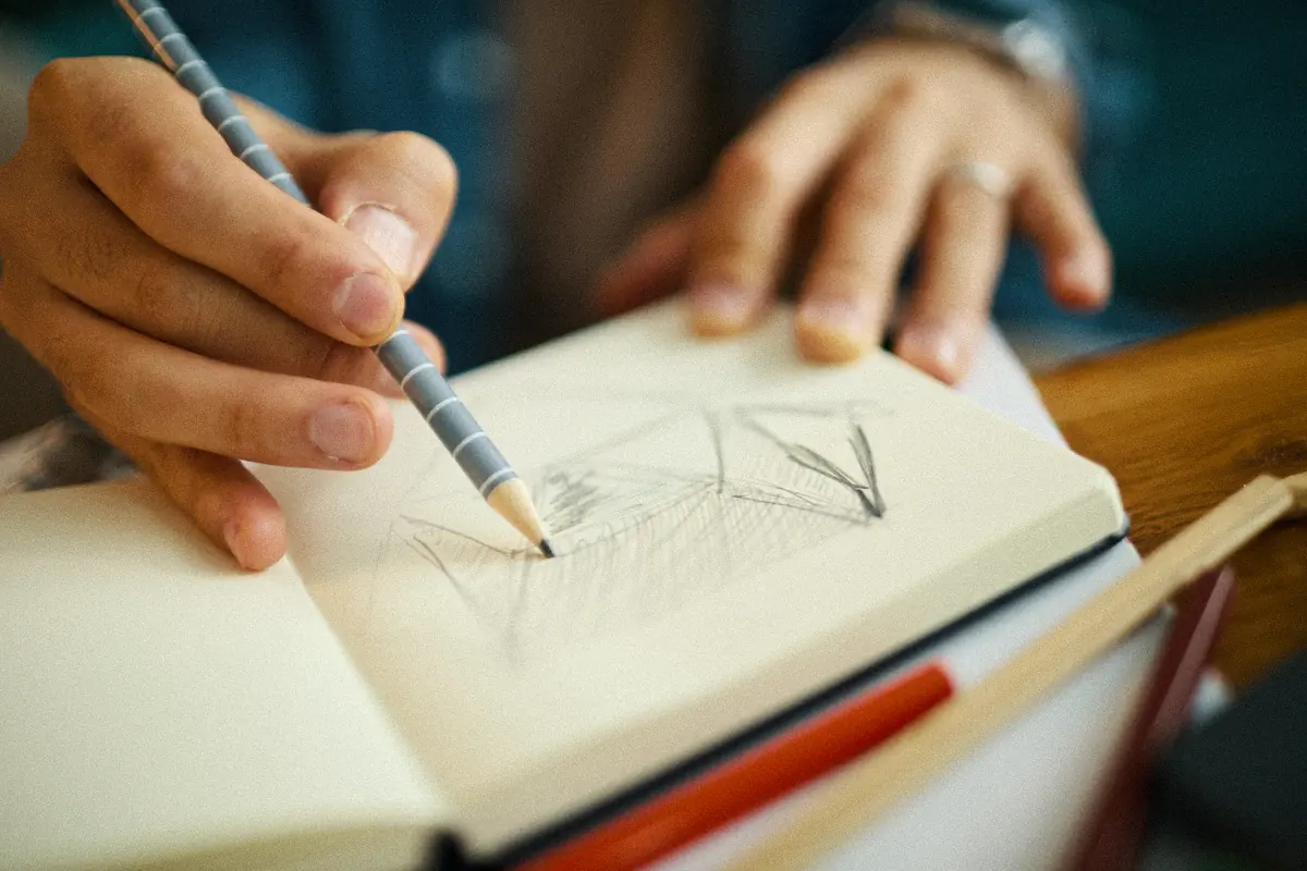 Main dessinant un logo au crayon dans un carnet : le travail que ne fait ni un générateur de logo gratuit ni une IA