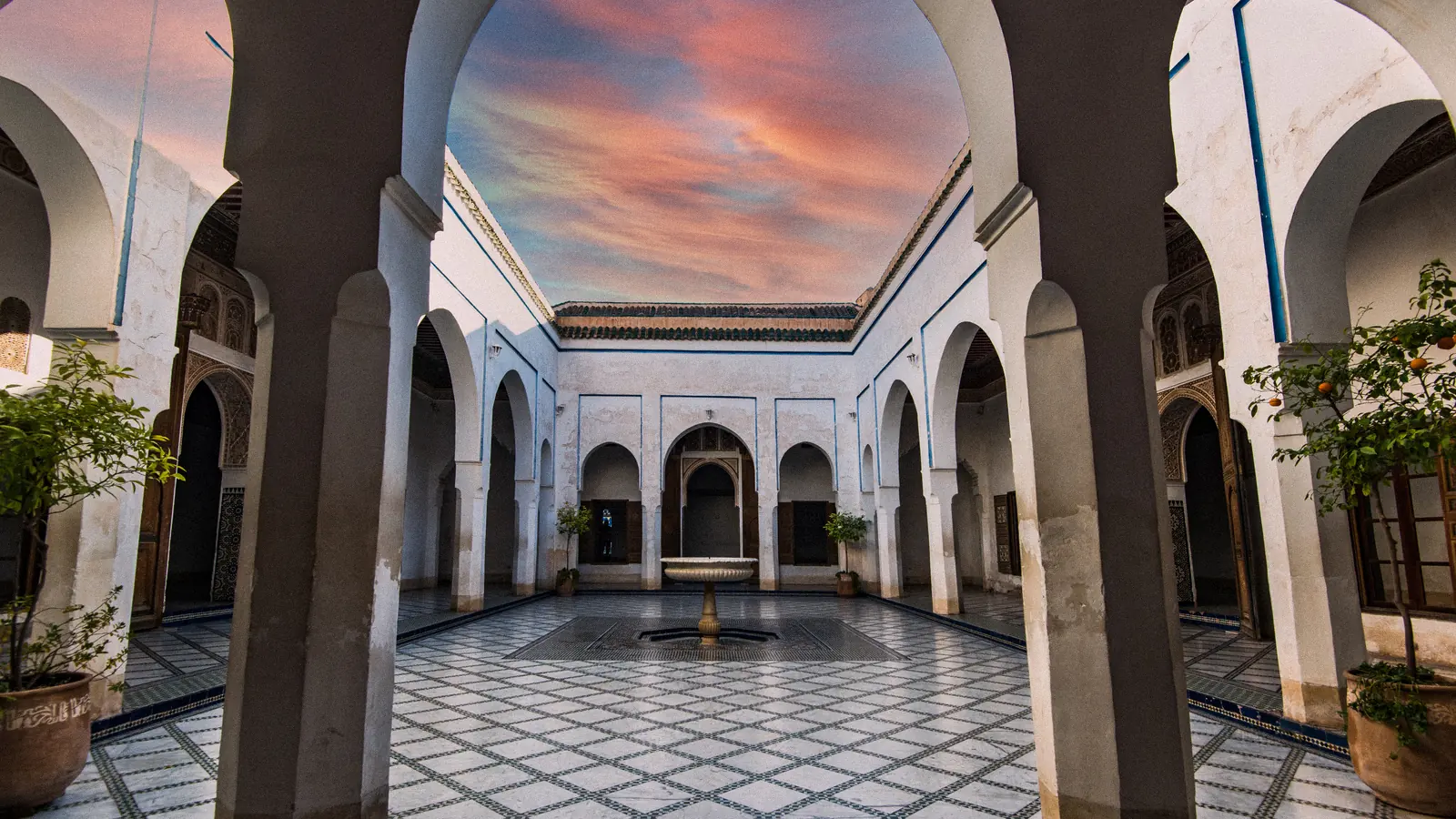 Courtyard of the Bahia Palace in Marrakech, zellige floor, arches and fountain under a sunset sky: a Marrakech photoshoot location