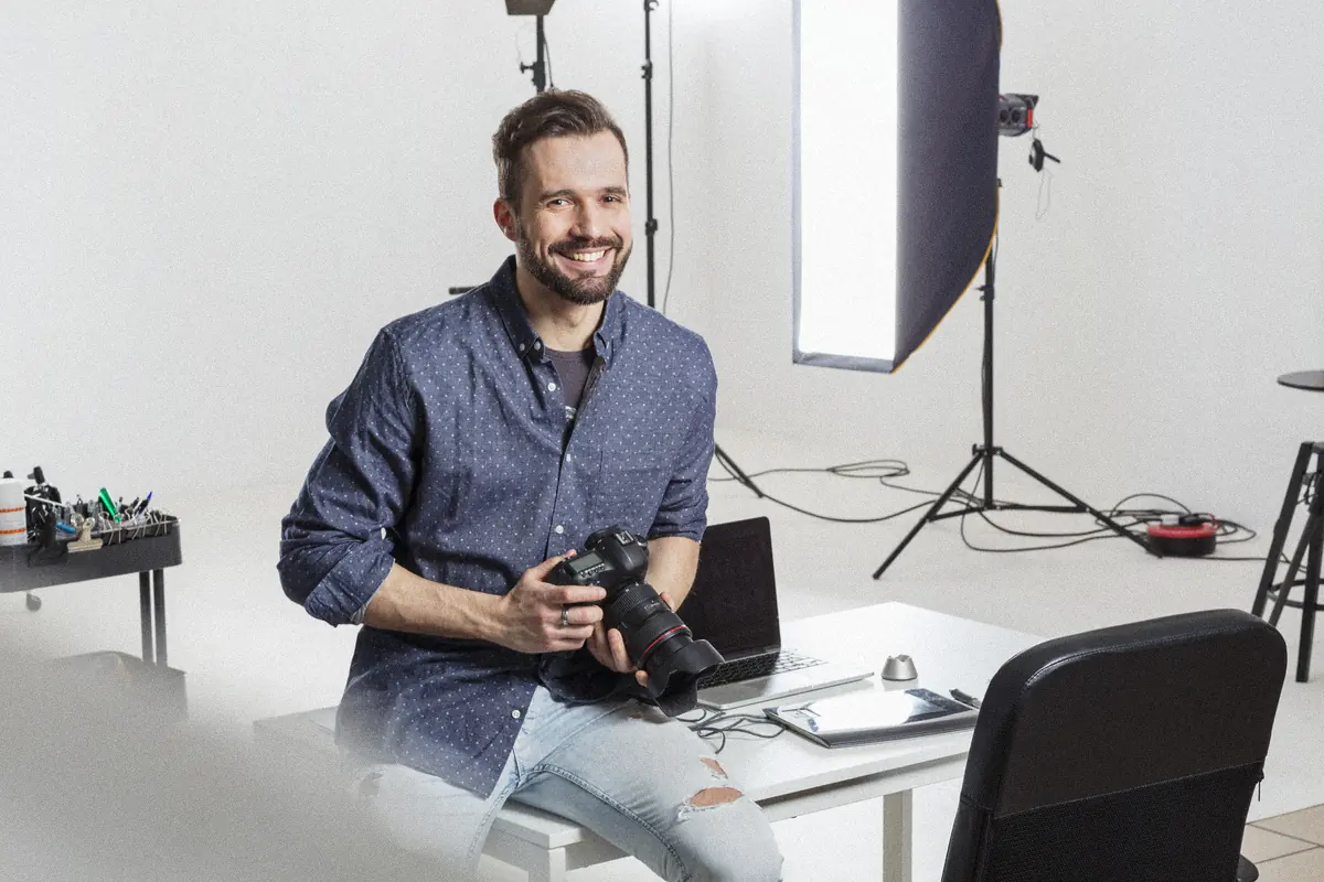 Photographe souriant dans son studio, appareil en main, devant une boîte à lumière : séance de portrait corporate