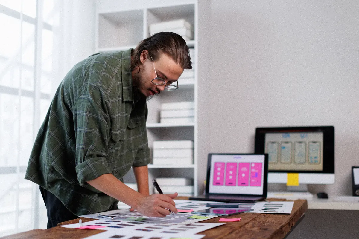 Designer vérifiant des maquettes d’écrans à son bureau pendant la refonte d’un site internet