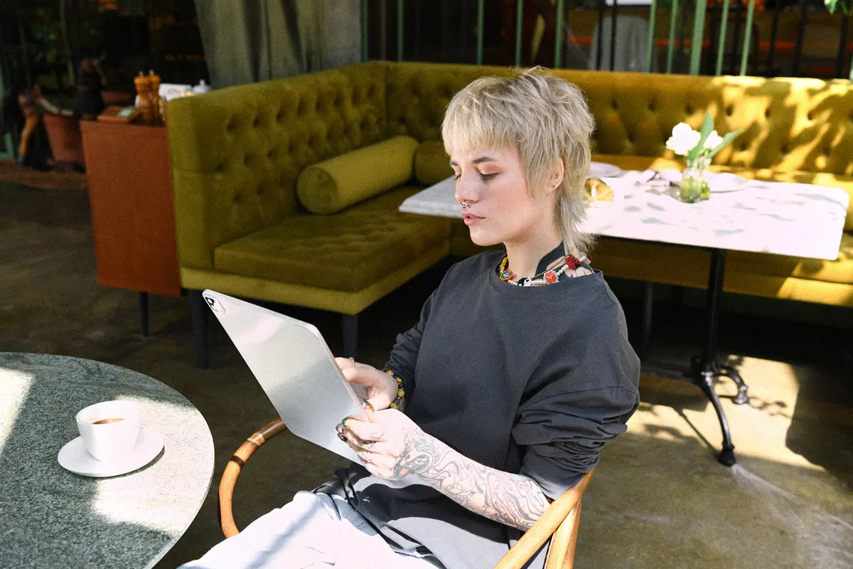 Jeune femme travaillant sur une tablette dans un café ensoleillé : créer soi-même son site internet gratuit