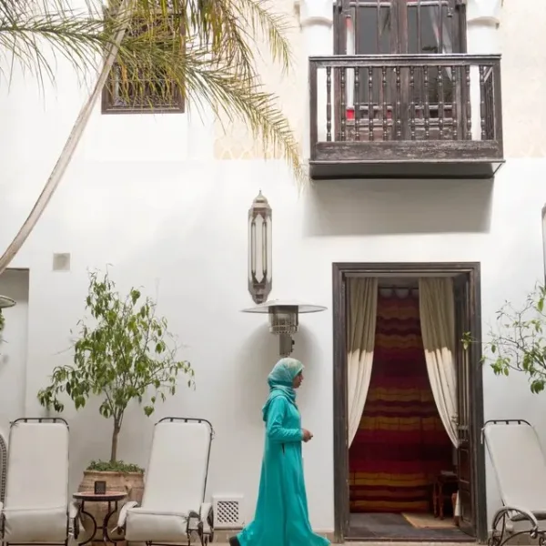 A woman in a turquoise dress walking along the pool of a white riad courtyard