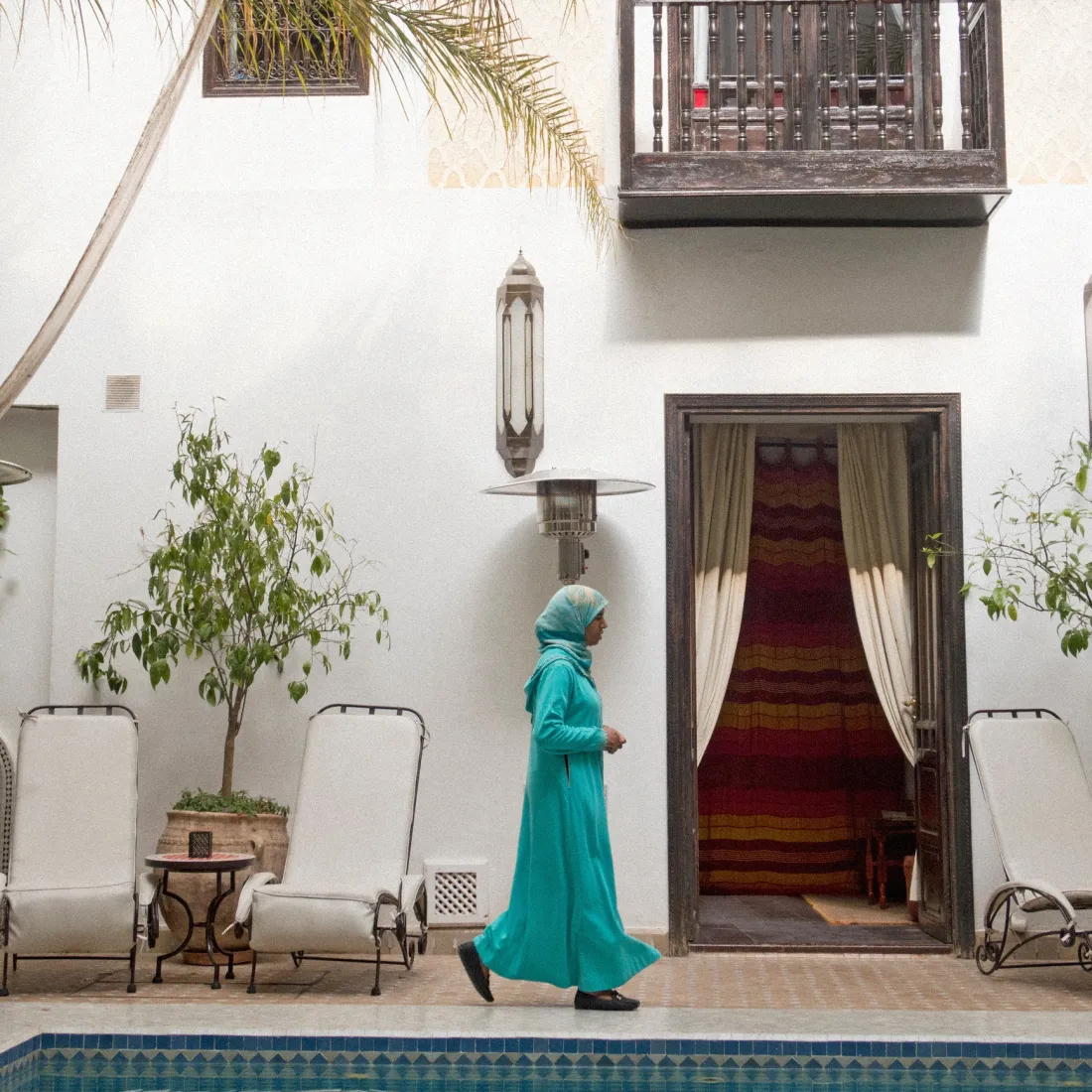 Woman in a turquoise dress walking along the pool of a white riad in Marrakech