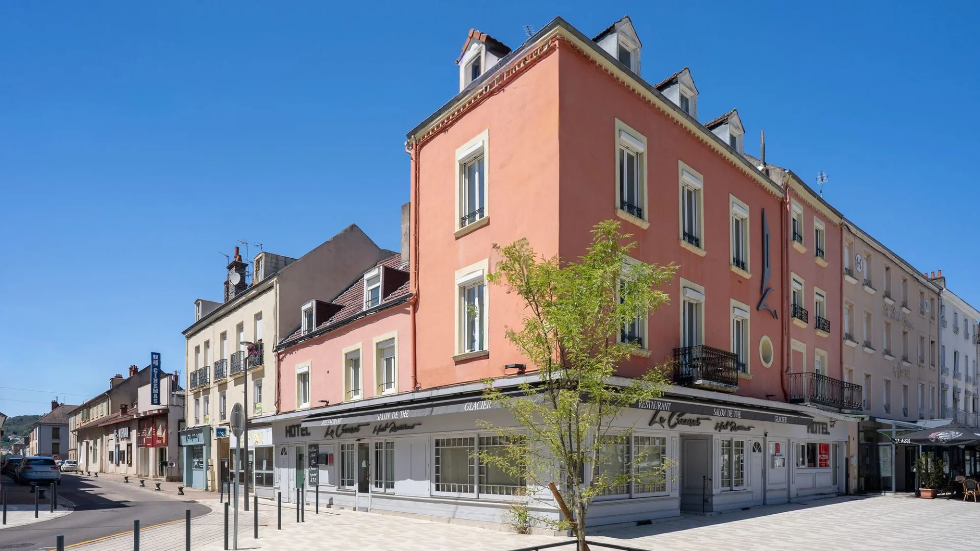 The Le Creusot Suites residence, a pink building on the corner of place Schneider in Le Creusot, under a blue sky