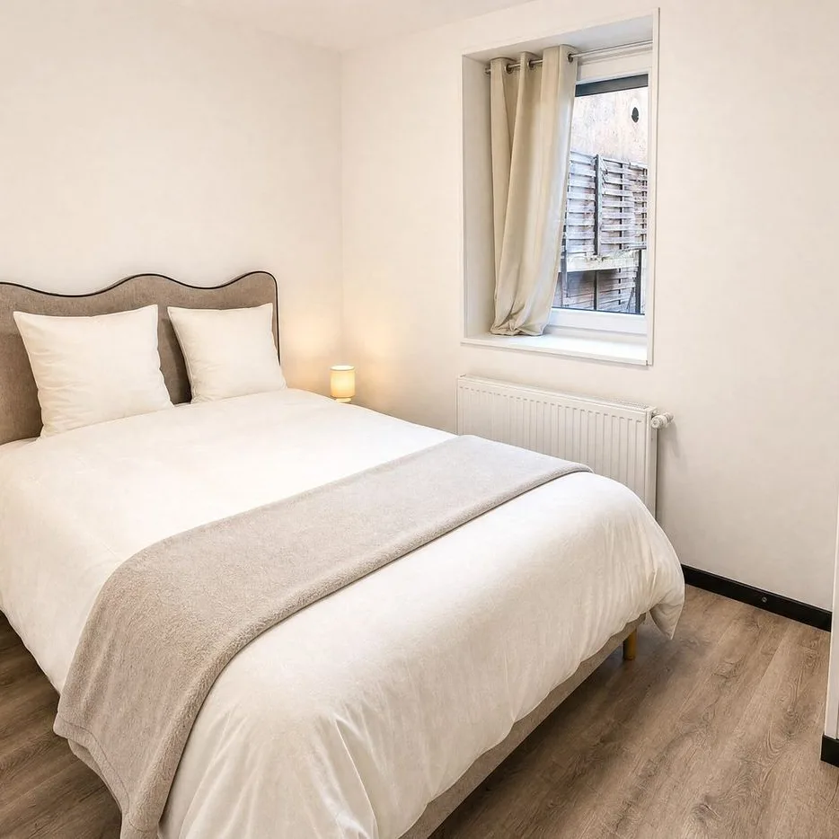 A bedroom of the suite: a double bed with a curved headboard, a window and light wood floors