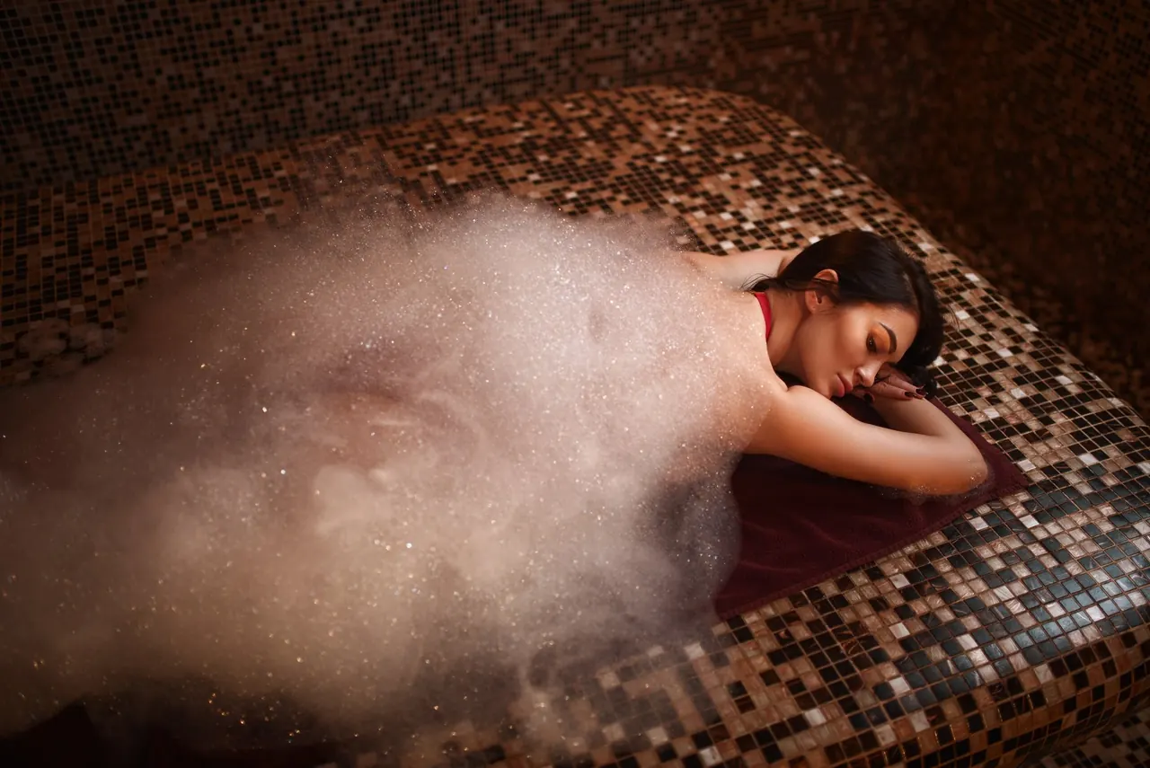 A woman resting on a warm mosaic platform in the steam