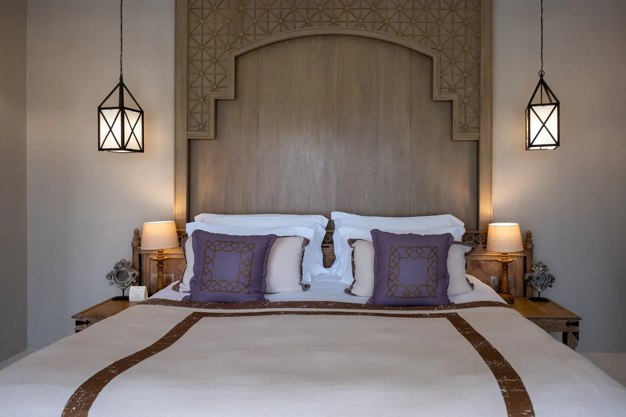 Bedroom with a carved wooden headboard, two lanterns and purple cushions